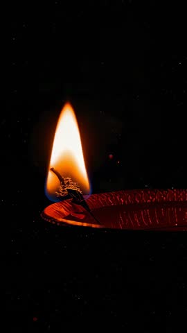 Vertical video glowing oil lamp flame with twisted wick flickering in deep dark background