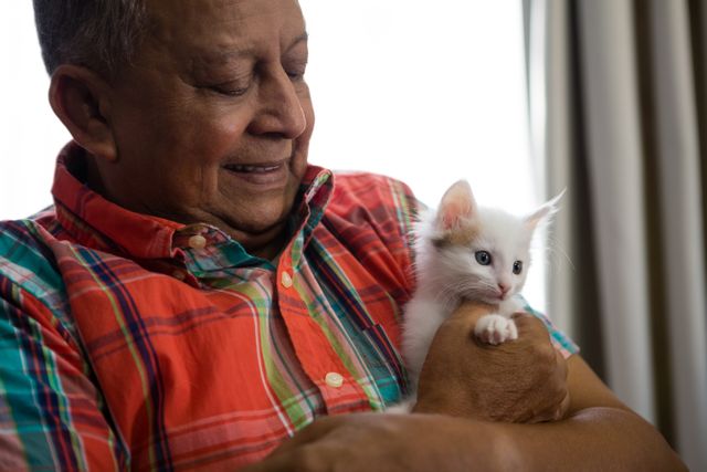 Happy senior man playing with kitten at nursing home