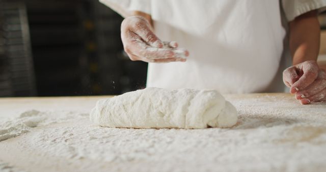 Baker's hands working with dough and flour in a kitchen environment. Image demonstrates the process of breadmaking, flour dusted on surfaces, making it perfect for articles on baking, cooking techniques, food blogs, culinary websites, and educational content involving baking instructions.