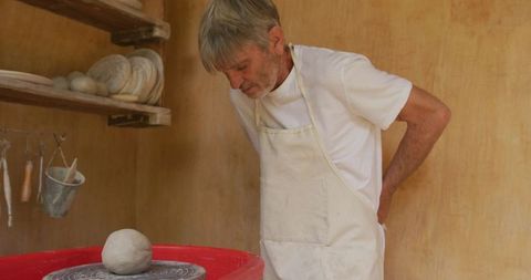 Senior man crafting pottery in workshop with studious expression
