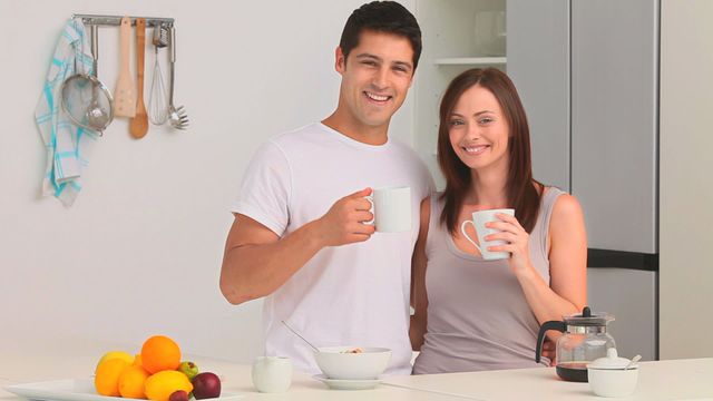 This video shows a smiling couple enjoying coffee together in a modern kitchen. They are holding coffee mugs and seem relaxed, creating a cozy atmosphere perfect for themes about home life, relationships, shared moments, and morning routines. It is ideal for use in lifestyle blogs, advertisements for kitchen appliances, coffee-related products, and articles promoting healthy relationships.