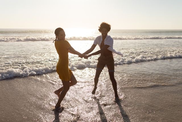 Couple holding hands and enjoying a playful moment on the beach during sunset. Ideal for use in travel brochures, romantic getaway promotions, lifestyle blogs, and advertisements focusing on relationships and leisure activities.