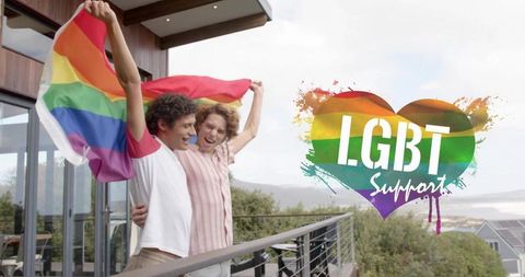 Young gay couple celebrating with pride flag on modern oceanfront deck lgbt support heart
