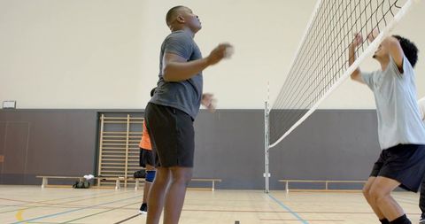 Diverse male volleyball players jumping and blocking at net on indoor gymnasium court