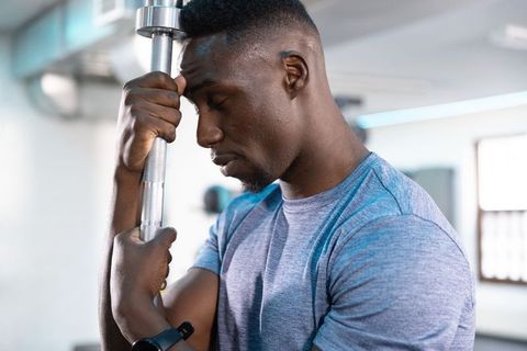 African American man resting on barbell in gym showing fatigue and focus