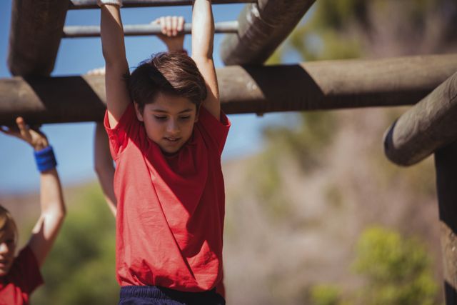 Children are participating in an outdoor obstacle course, climbing monkey bars as part of a boot camp training. This image can be used for promoting children's fitness programs, summer camps, physical education activities, and team-building exercises. It highlights teamwork, physical activity, and outdoor adventure.