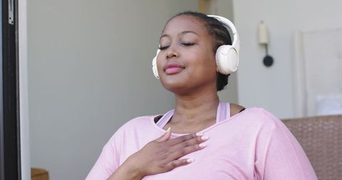 Mid adult african american woman meditating with headphones, relaxing on porch