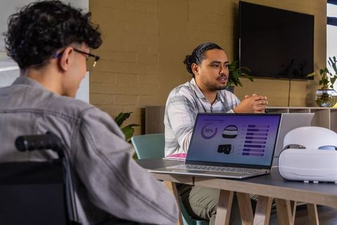 Diverse team presenting data to coworker in wheelchair during collaborative office meeting