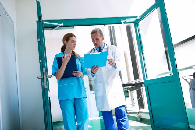Doctor and nurse standing in a hospital corridor, reviewing a medical report on a clipboard. Ideal for use in healthcare-related articles, medical websites, hospital brochures, and educational materials about medical teamwork and patient care.