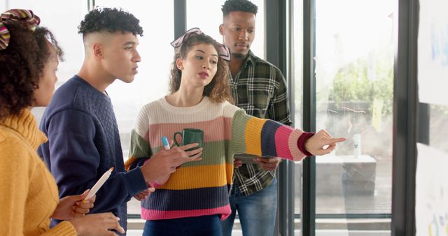 Diverse group of young professionals collaborating in an office, discussing ideas and planning a project. Useful for illustrating teamwork, creativity in a business environment, office settings, and corporate teamwork concepts.