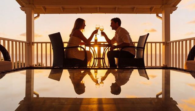 Couple clinking wine glasses on ocean terrace at sunset with reflective pool