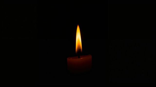 Single pillar candle burning with warm flame and soft halo on dark minimalist background