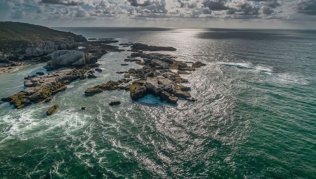Turquoise surf flowing around rocky outcrop stretching toward horizon on rugged coast