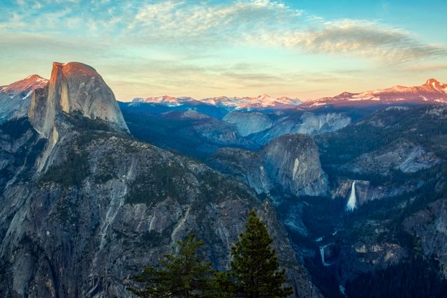 Half Dome in Yosemite National Park at sunset with a stunning view of surrounding mountains and valleys. The serene sky is covered with clouds tinged by the sunset hues. Ideal for use in travel magazines, environmental websites, posters, and nature calendars.