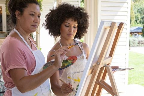 Mature instructor guiding young learner in outdoor painting session