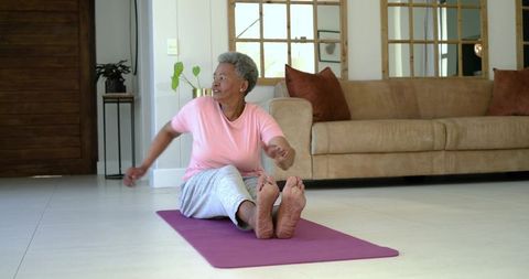 Senior woman stretching on yoga mat in living room practicing seated twist for wellness