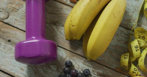 Purple dumbbell with bananas, blueberries and measuring tape on rustic wood