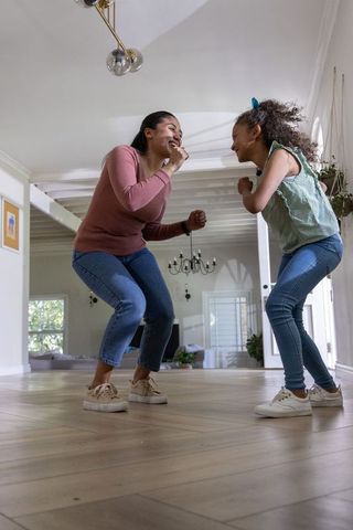 Joyful woman and girl dancing on hardwood floor in bright modern living room