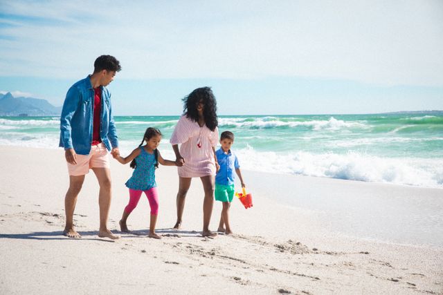 Full length of parents holding hands with children while walking on shore at beach during sunny day. family, lifestyle and weekend.