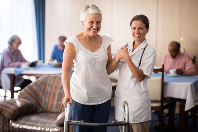 Portrait of smiling senior woman holding hands with female doctor by walker at retirement nursing home
