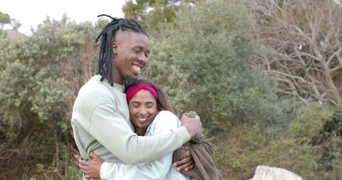 Diverse couple embracing and smiling in nature with denim jacket and red headband