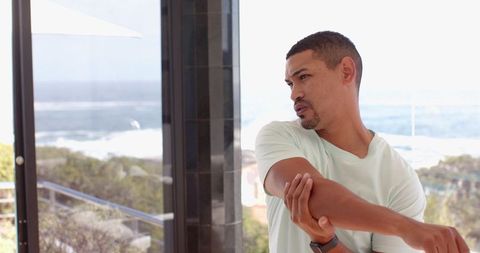 Mid adult man stretching on seaside terrace with smartwatch