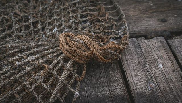 Knotted rope and weathered fishing net on rustic wooden dock with barnacle texture
