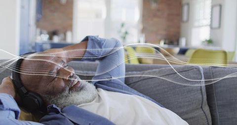 Mature man relaxing on sofa listening to music with headphones and sound wave overlay