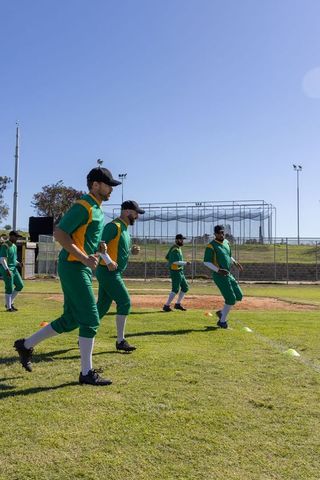 Baseball team performing warm-up stride drills on grassy field with cones and batting cage