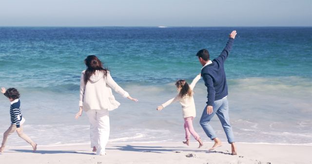 Picture shows a family of four having fun on a sandy beach with the ocean in the background. Parents and children are playing, smiling, and enjoying their time together, showcasing a joyful holiday moment. Ideal use for travel agency promotions, family-oriented products, and vacation brochures to portray happiness and family bonding.