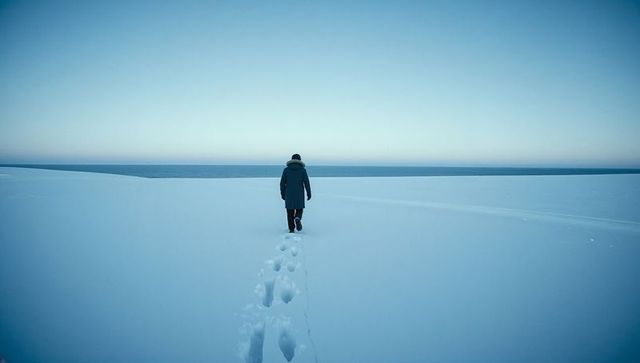 Solitary figure walking across snow toward sea at arctic blue horizon