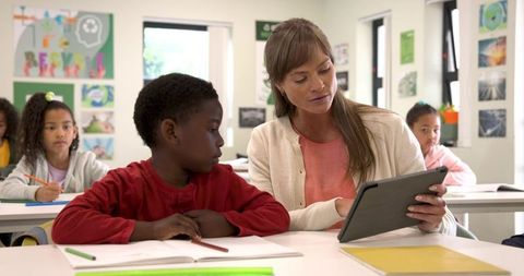 Caring teacher with diverse students using tablet for classroom learning
