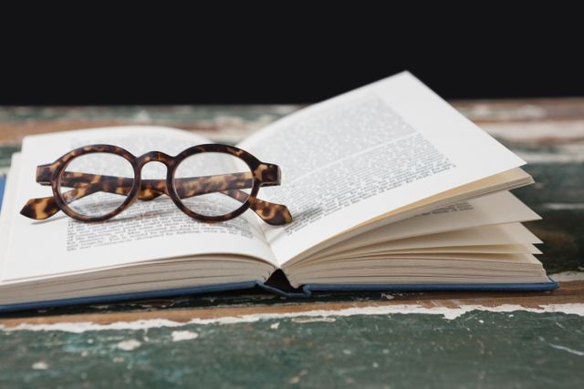 Vintage glasses resting on an open book on a rustic wooden table. Ideal for themes related to reading, education, literature, and intellectual pursuits. Perfect for use in educational materials, library promotions, book clubs, and literary blogs.