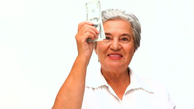 Mature woman expressing joy while holding dollar bills, symbolizing financial success and independence. Useful for articles or content about financial planning, retirement savings, senior independence, or banking advertisements.