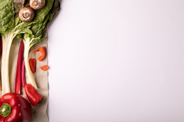 Overhead view of fresh vegetables including leafy greens, red pepper, and mushrooms on a white background. Ideal for use in healthy eating promotions, organic food advertisements, vegetarian and vegan recipe blogs, and nutrition-focused content.