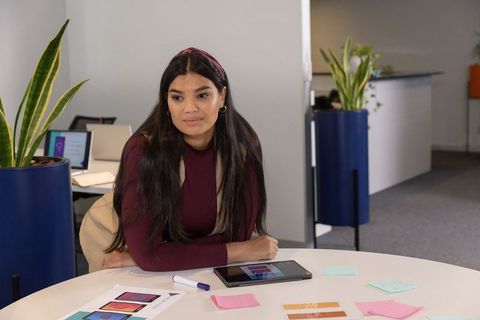 Designer leaning on table reviewing tablet and color swatches in modern office workspace