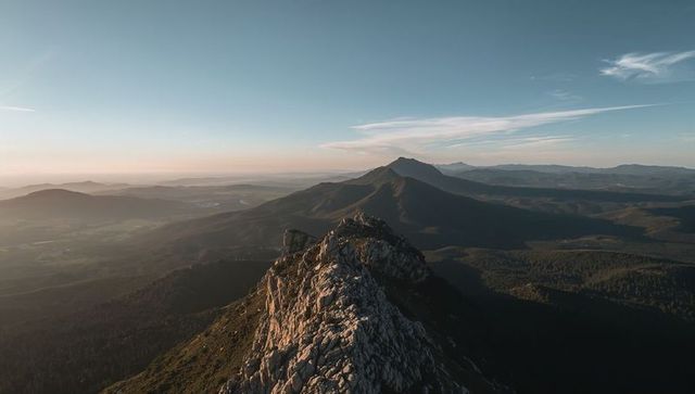 Sunlight illuminating rugged rocky ridge stretching toward distant mountain peak at sunrise