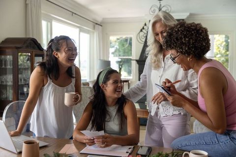 Multigenerational women collaborating over papers and laptop around sunny wood dining table