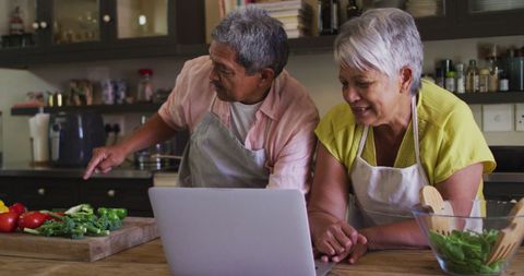 Senior Couple Cooking Together at Home Using Laptop