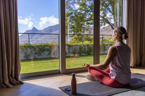 Woman meditating by glass doors with mountain view, yoga mindfulness and morning calm