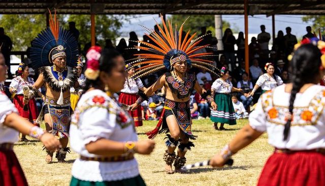 Mexican aztec dancer with orange-black feather headdress and colorful embroidered costumes