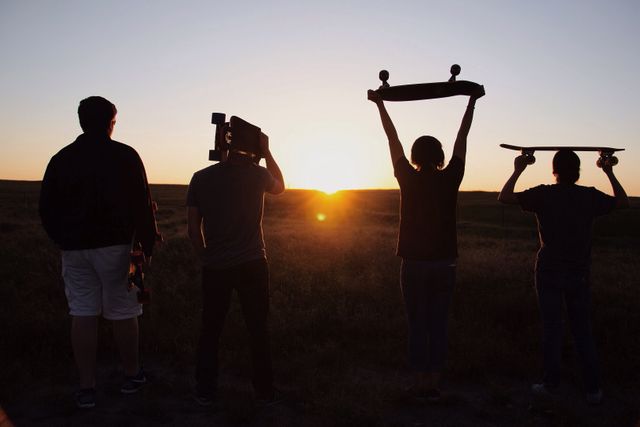 Four teenagers, silhouetted against sunset, holding skateboards in countryside. Emphasizing adventure, friendship, recreation, outdoor lifestyle ideal for campaigns focused on youth culture, active living, travel, and sports.