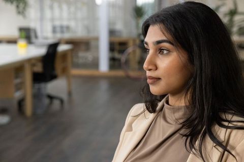 Confident indian professional woman looking ahead in modern open office with bicycle