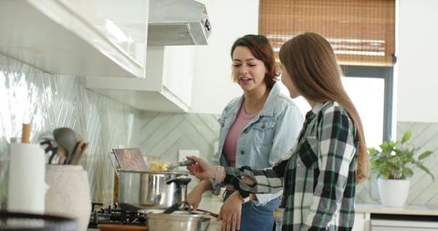African american friends cooking together in bright modern kitchen stirring pot laughing