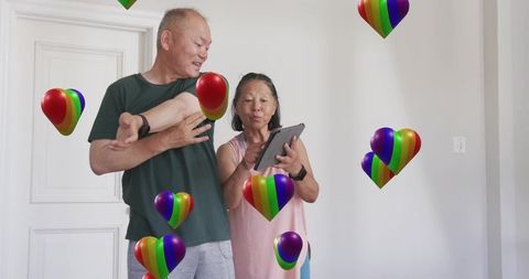 Older couple using tablet at home showing floating rainbow hearts