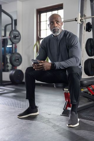 Fit african american man resting on gym bench checking smartphone between workout sets