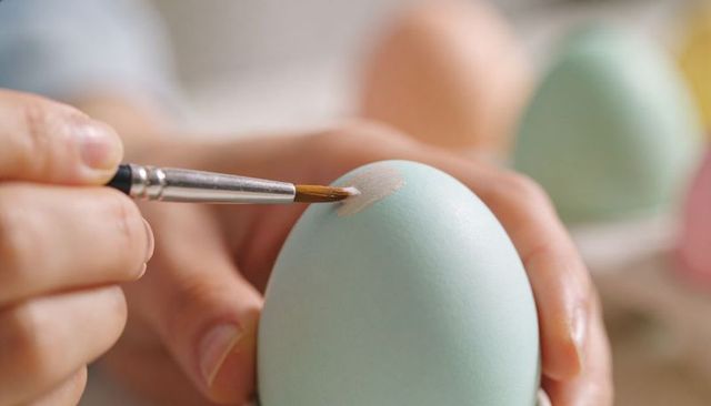 Hand painting pastel blue easter egg with fine brush closeup delicate crafting scene