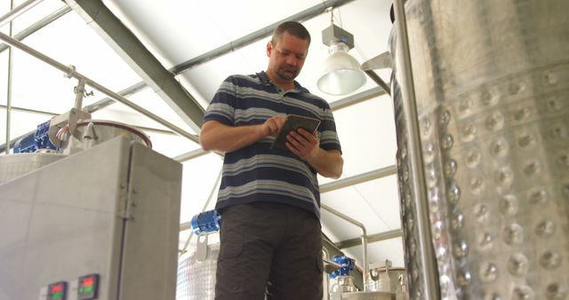 Man in brewery checking tablet amidst large metal equipment - Download Free Stock Images Pikwizard.com