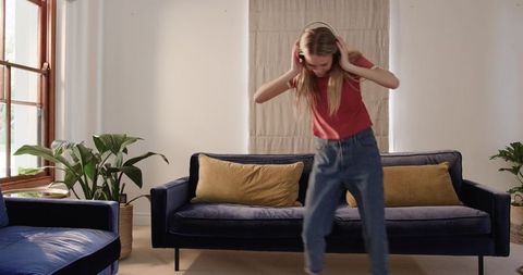 Young woman adjusting over-ear headphones while leaning in cozy sunlit living room