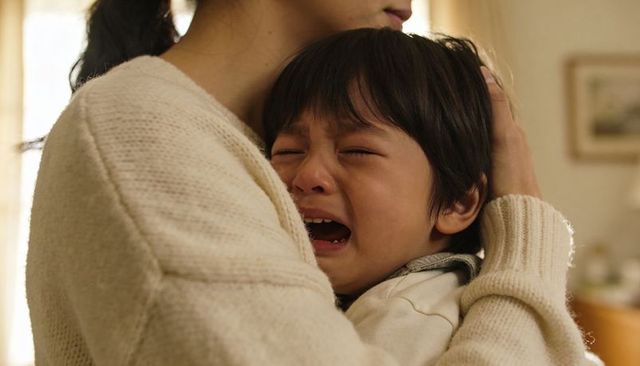 Mother comforting crying child in warm home embrace, tender parental care and empathy